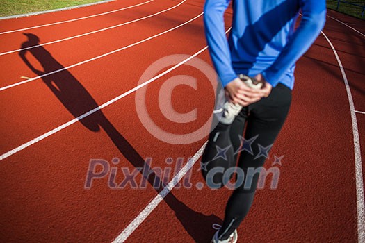 Young woman stretching before her run casts a shadow on the track Young woman stretching before her run casts a shadow on the track