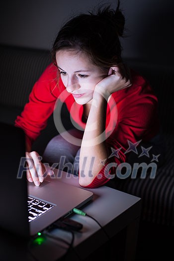 Young woman working on her laptop late at night - burning the midnight oil, trying to finish her paper