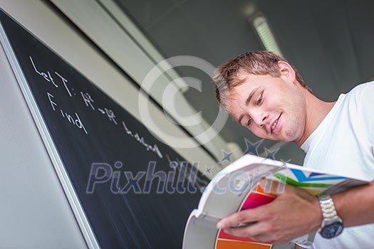 Handsome college student solving a math problem during math class in front of the blackboard/chalkboard (color toned image) Handsome college student solving a math problem during math class in front of the blackboard/chalkboard (color toned image)