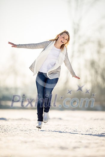 Young woman ice skating outdoors on a pond on a freezing winter day (color toned image; motion blurred image)