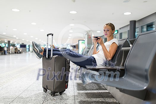 Young female passenger at the airport, using her tablet computer while waiting for her flight (color toned image) Young female passenger at the airport, using her tablet computer while waiting for her flight (color toned image)