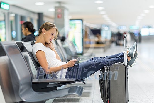 Young female passenger at the airport, using her tablet computer while waiting for her flight (color toned image) Young female passenger at the airport, using her tablet computer while waiting for her flight (color toned image)