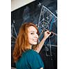 Portrait of a pretty young college student writing on the blackboard during a maths class (color toned image)