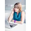 Pretty, young woman at an office, using a laptop and her smartphone