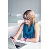 Pretty, young woman at an office, using a laptop and her smartphone