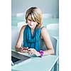 Pretty, young woman at an office, using a laptop and her smartphone