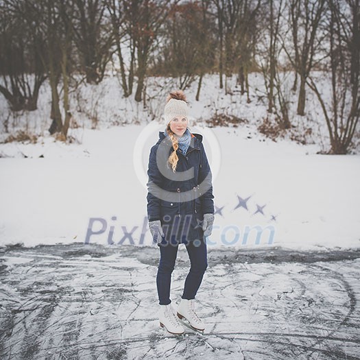 Young woman ice skating outdoors on a pond on a freezing winter day (color toned image; motion blurred image)