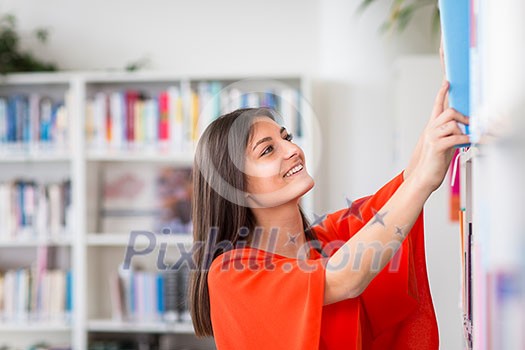 Pretty, young college student looking for a book in the library, studying for her exam Pretty, young college student looking for a book in the library, studying for her exam
