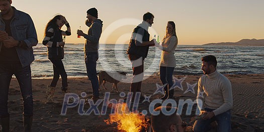 Happy Carefree Young Friends Having Fun And Drinking Beer By Bonefire On The Beach As The Sun Begins To Set Happy Carefree Young Friends Having Fun And Drinking Beer By Bonefire On The Beach As The Sun Begins To Set