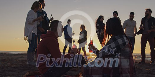 Happy Carefree Young Friends Having Fun And Drinking Beer By Bonefire On The Beach As The Sun Begins To Set Happy Carefree Young Friends Having Fun And Drinking Beer By Bonefire On The Beach As The Sun Begins To Set
