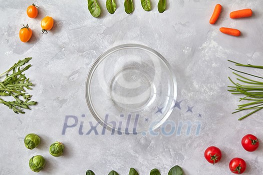 Empty glass plate and fresh vegetables on a gray concrete background, the first stage of salad cooking, a photo from a series of turn-based salad cooking. Top view, flat lay Empty glass plate and fresh vegetables on a gray concrete background, the first stage of salad cooking, a photo from a series of turn-based salad cooking. Top view, flat lay