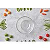 Empty glass plate and fresh vegetables on a gray concrete background, the first stage of salad cooking, a photo from a series of turn-based salad cooking. Top view, flat lay