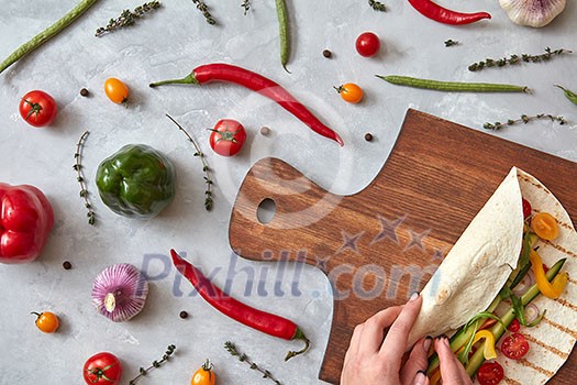 A woman makes a burrito with fresh vegetables on a wooden board. A step-by-step recipe for cooking. Top view, flat lay. A woman makes a burrito with fresh vegetables on a wooden board. A step-by-step recipe for cooking. Top view, flat lay.