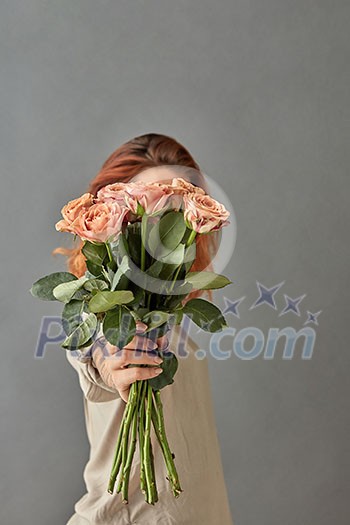 A bouquet of beige roses in a girl's hand on a gray background. Mothers Day. A bouquet of beige roses in a girl's hand on a gray background. Mothers Day.