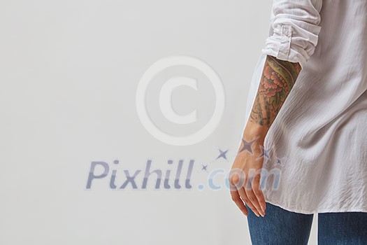 View from the back of a girl in jeans, a white shirt and with a tattoo on her hands on a gray background. Copy space View from the back of a girl in jeans, a white shirt and with a tattoo on her hands on a gray background. Copy space