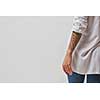 View from the back of a girl in jeans, a white shirt and with a tattoo on her hands on a gray background. Copy space