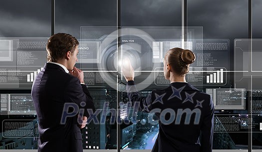 Rear view of businessman and businesswoman touching icon of digital screen Rear view of businessman and businesswoman touching icon of digital screen