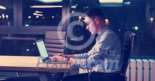 Young man working on laptop at night in dark office. The designer works in the later time. Young man working on laptop at night in dark office. The designer works in the later time.