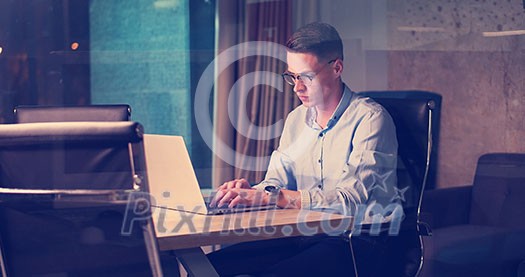 Young man working on laptop at night in dark office. The designer works in the later time. Young man working on laptop at night in dark office. The designer works in the later time.