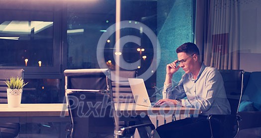 Young man working on laptop at night in dark office. The designer works in the later time. Young man working on laptop at night in dark office. The designer works in the later time.