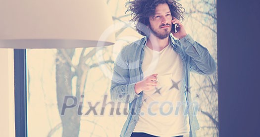 Handsome casual young man drinking coffee and using a mobile phone at home Handsome casual young man drinking coffee and using a mobile phone at home