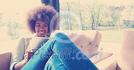 Young african american woman at home relaxing in her luxury lliving room reading a digital tablet PC surf internet and work Young african american woman at home relaxing in her luxury lliving room reading a digital tablet PC surf internet and work