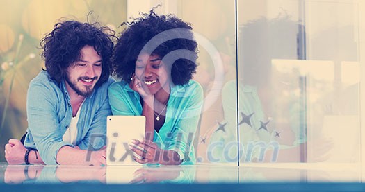 Happy young multiethnic couple lying on floor having fun using Digital Tablet