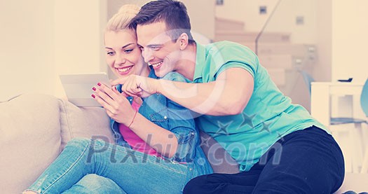 Young couple relaxing at luxurious home with tablet computers reading in the living room on the sofa couch. Young couple relaxing at luxurious home with tablet computers reading in the living room on the sofa couch.