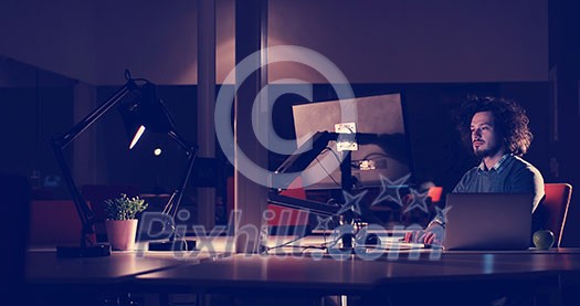 Young man working on computer at night in dark office. The designer works in the later time. Young man working on computer at night in dark office. The designer works in the later time.