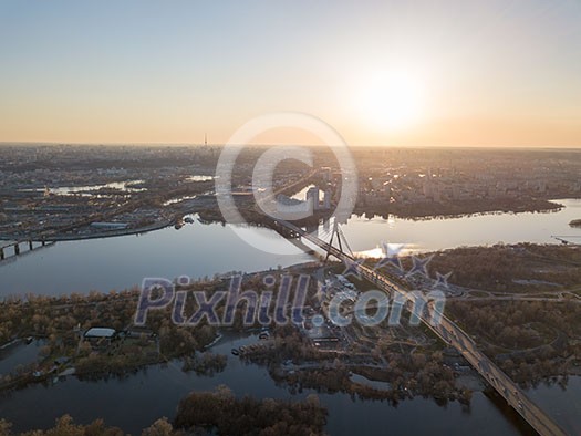 Aerial view of the bridge and the road over the Dnepr River over a green island in the middle of the river. City of Kiev at sunset, Ukraine. Aerial view of the bridge and the road over the Dnepr River over a green island in the middle of the river. City of Kiev at sunset, Ukraine.