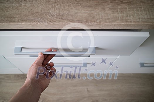 Man hand opening white drawer for cutlery, focus on steel handle of kitchen counter Man hand opening white drawer for cutlery, focus on steel handle of kitchen counter