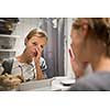 Groggy, young woman yawning in front of her bathroom mirror in the morning - trying to wake up and get ready for work (color toned image; shallow DOF)