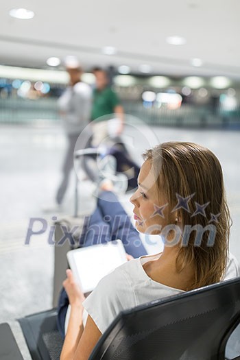 Young female passenger at the airport, using her tablet computer while waiting for her flight (color toned image) Young female passenger at the airport, using her tablet computer while waiting for her flight (color toned image)