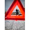 Realy angry young woman in a road distress situation - setting up a warning triangle and calling for assistance after her car broke down in the middle of nowhere on a freezing winter day