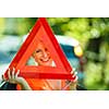 Young female driver wearing a high visibility vest, calling the roadside service/assistance after her car has broken down