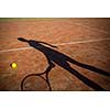 shadow of a tennis player in action on a tennis court (conceptual image with a tennis ball lying on the court and the shadow of the player positioned in a way he seems to be playing it)