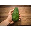 Half an avocado in a hand in front of wooden kitchen table