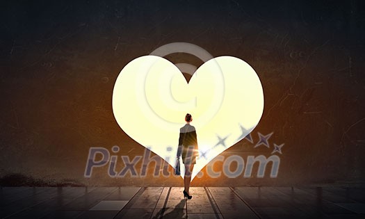 Businesswoman standing with back in light of heart door Businesswoman standing with back in light of heart door