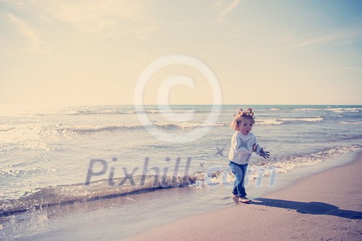 Adorable little girl having fun at beach during autumn day. Happy baby by the sea or ocean Adorable little girl having fun at beach during autumn day. Happy baby by the sea or ocean