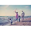 young family with kids resting and having fun with a kite at beach during autumn day