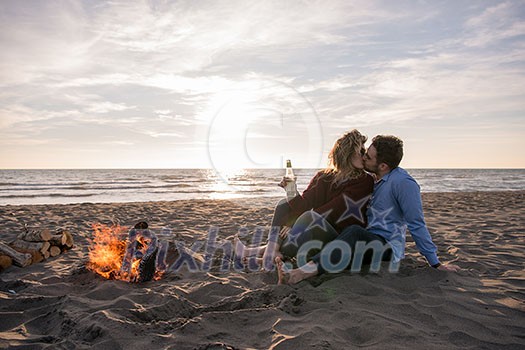 Young Couple Relaxing By The Fire, Drinking A Beer Or A Drink From The Bottle on the beach at autumn day Young Couple Relaxing By The Fire, Drinking A Beer Or A Drink From The Bottle on the beach at autumn day