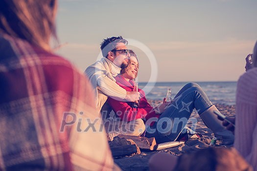 Young Couple enjoying with friends Around Campfire on The Beach At sunset drinking beer