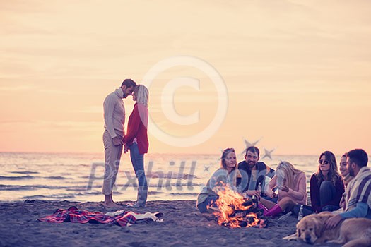 Young Couple enjoying with friends Around Campfire on The Beach At sunset drinking beer Young Couple enjoying with friends Around Campfire on The Beach At sunset drinking beer