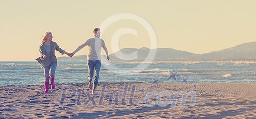 Young couple having fun walking and hugging on beach during autumn sunny day