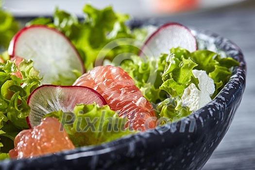 Freshly prepared dietary vegetarian salad with natural organic vegetables, citrus fruits, in a black plate on a gray table with copy cpace. Healthy detox clean eating.