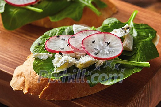 Ciabatta toasts with soft cottage cheese, slices of radish, fresh spinach, flax seeds on wooden background. Healthy vegetarian snack. Ciabatta toasts with soft cottage cheese, slices of radish, fresh spinach, flax seeds on wooden background. Healthy vegetarian snack.