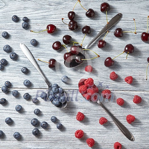 Colorfiul pattern of three spoons with various berries on a gray wooden background. Concept of healthy organic eating Colorfiul pattern of three spoons with various berries on a gray wooden background. Concept of healthy organic eating