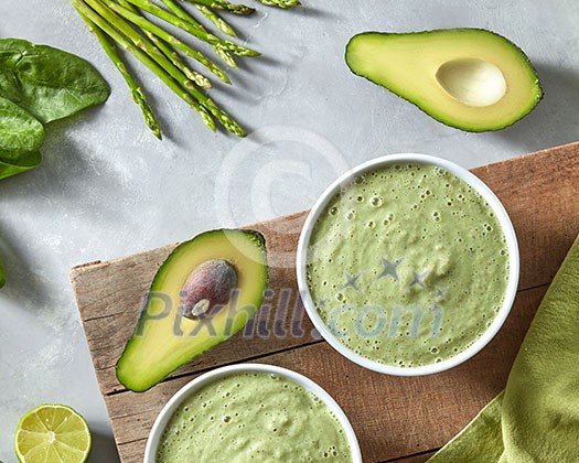 Homemade green healthy smoothies from spinach, avocado and asparagus in a bowl on a wooden board with a green napkin on a concrete background Homemade green healthy smoothies from spinach, avocado and asparagus in a bowl on a wooden board with a green napkin on a concrete background