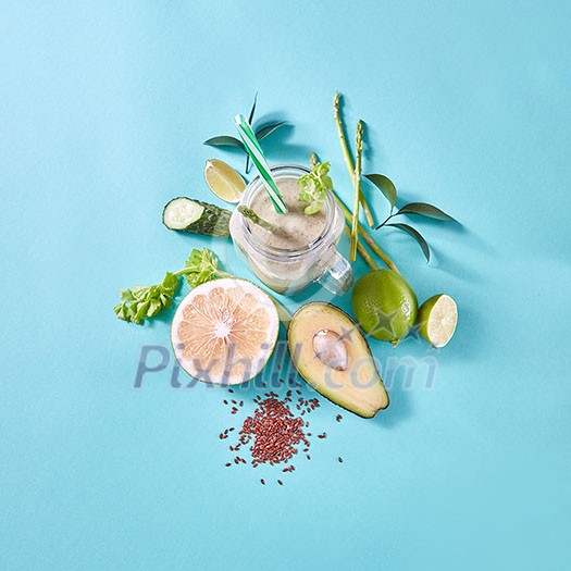 Organic freshly picked vegetables and fruits for preparing healthy vegetarian smoothie in a glass jar on blue paper background with copy space. Flat lay.