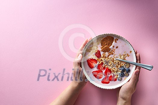 Healthy smoothie in white bowl with natural fruits, oat flakes and biscuits with woman's hands holding a bowl on pink background. Superfoods, natural detox, diet and healthy food. Flat lay Healthy smoothie in white bowl with natural fruits, oat flakes and biscuits with woman's hands holding a bowl on pink background. Superfoods, natural detox, diet and healthy food. Flat lay